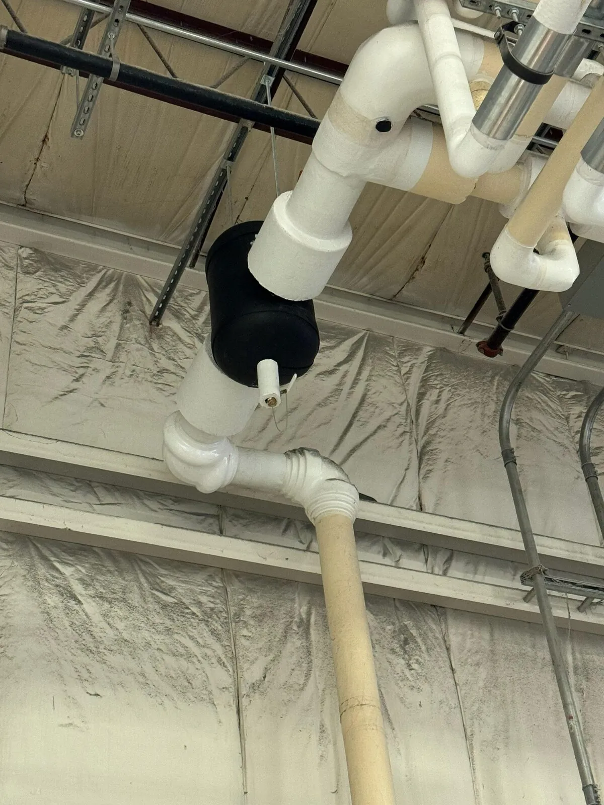 White PVC-jacketed insulated piping fittings at industrial ceiling