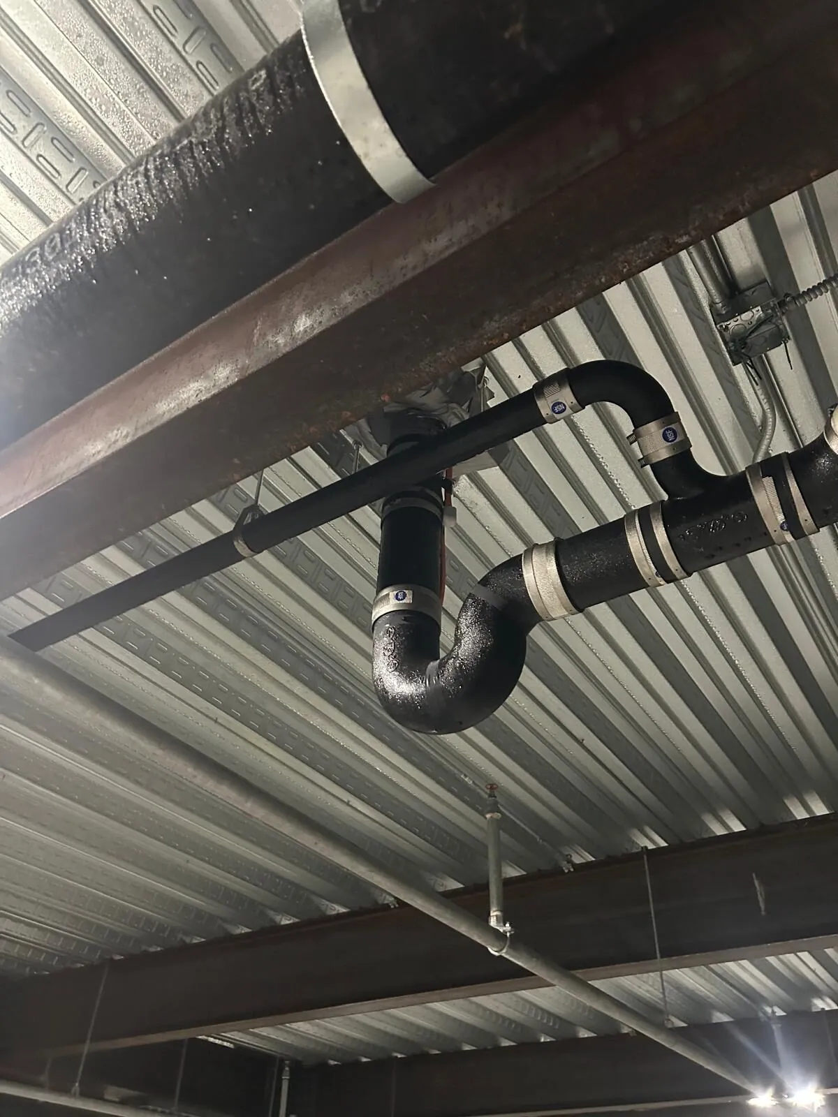 Black-jacketed insulated steel piping at structural beam penetration